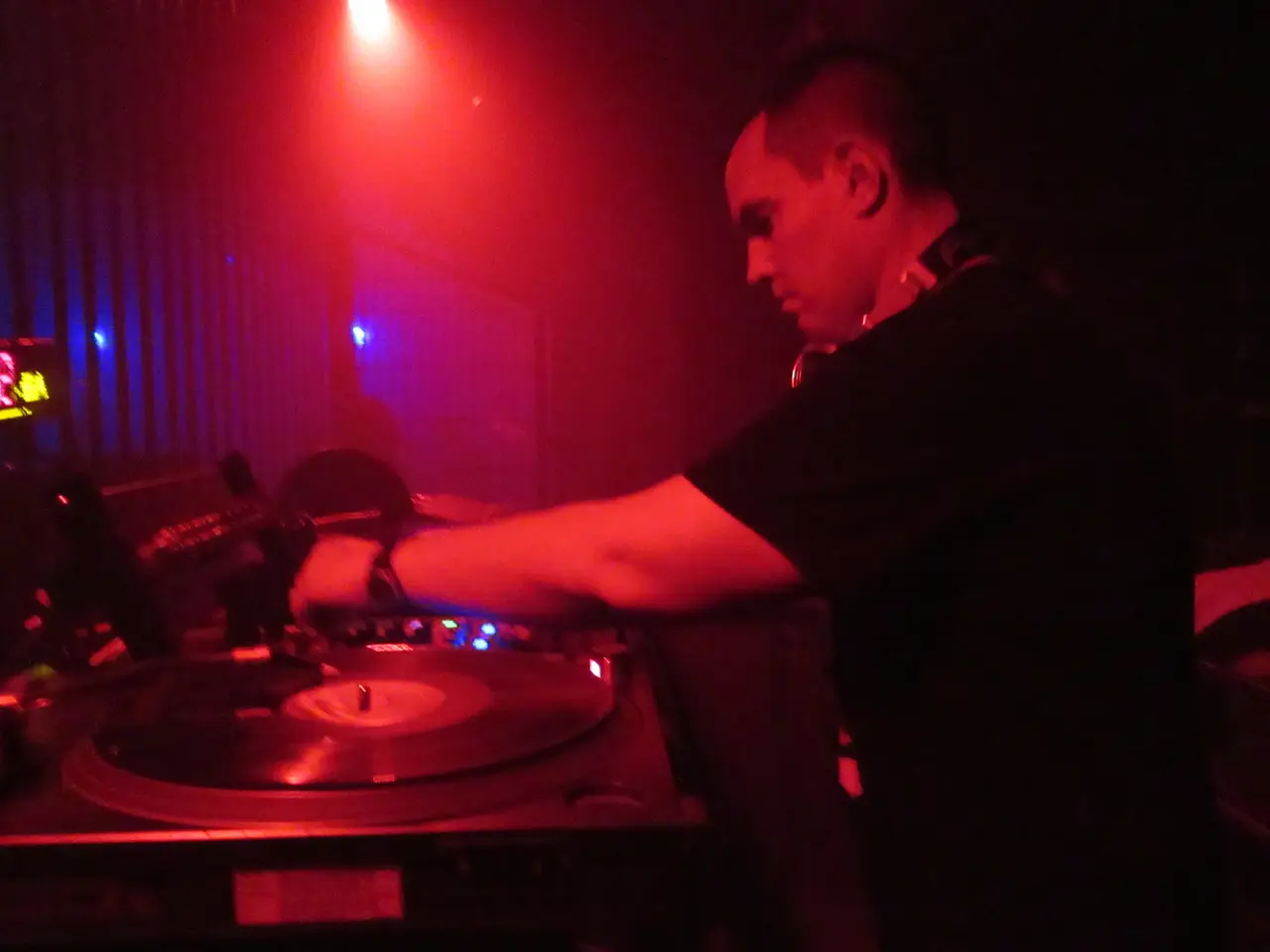 Primer plano del brazo de un DJ sobre un plato de vinilo, con luz roja y azul.