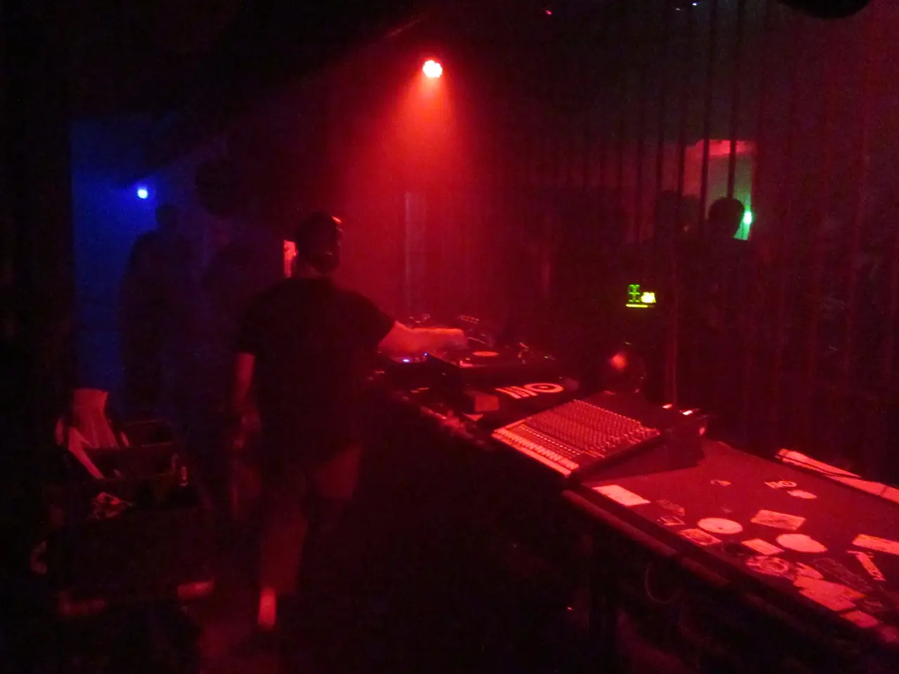DJ de espaldas mezclando en una cabina oscura con luz roja y azul.