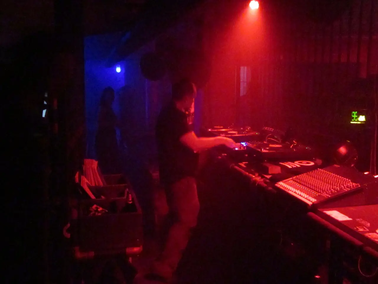 DJ con audífonos en primer plano sobre un plato de vinilo, con luz roja de fondo.