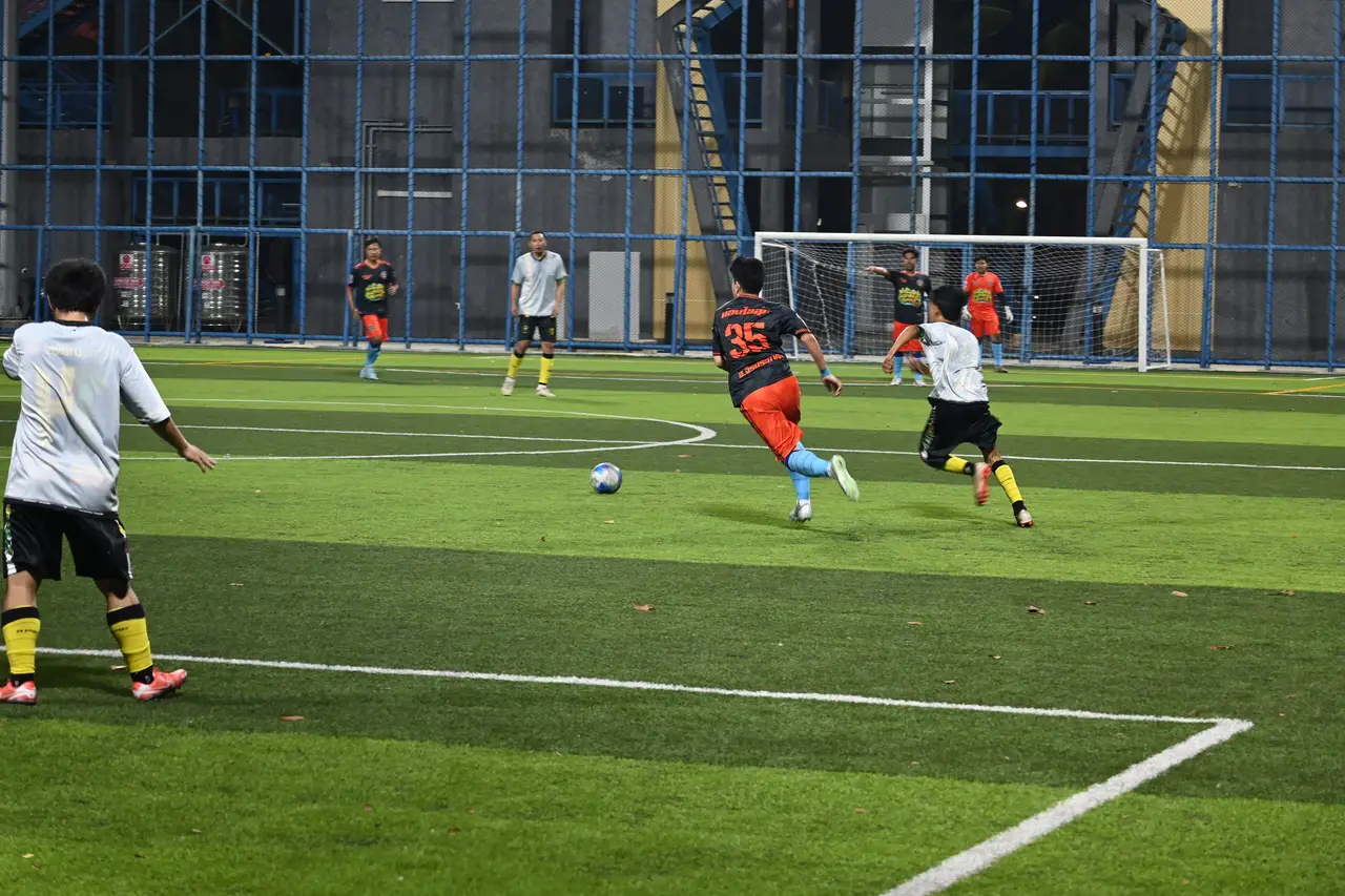 Jugadores disputando un balón en una cancha sintética cercada, de noche.
