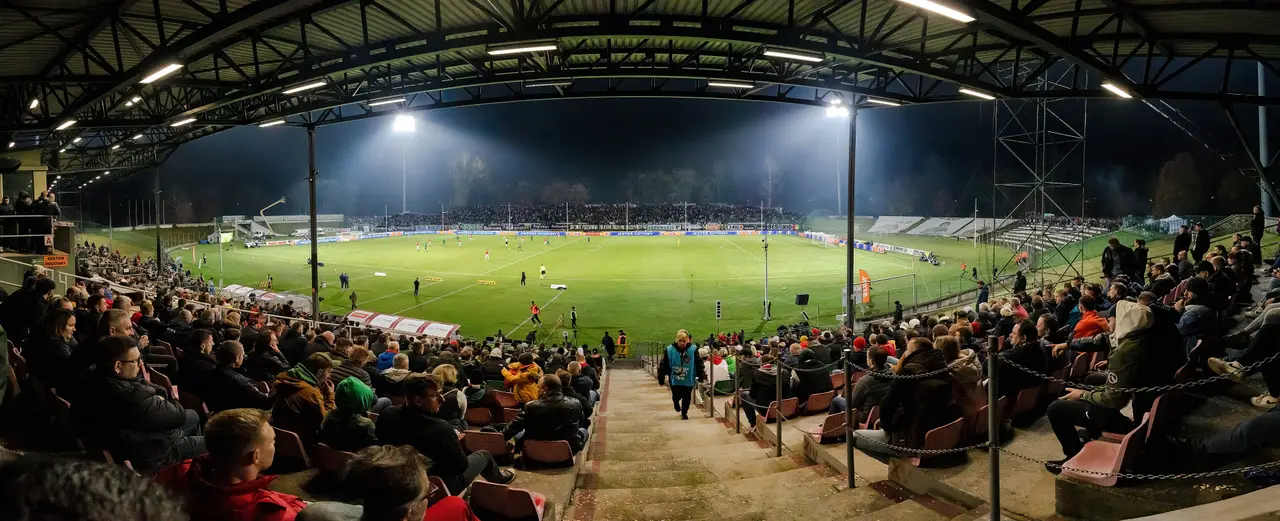 Panorámica de un estadio techado de noche, con reflectores y público en las gradas.
