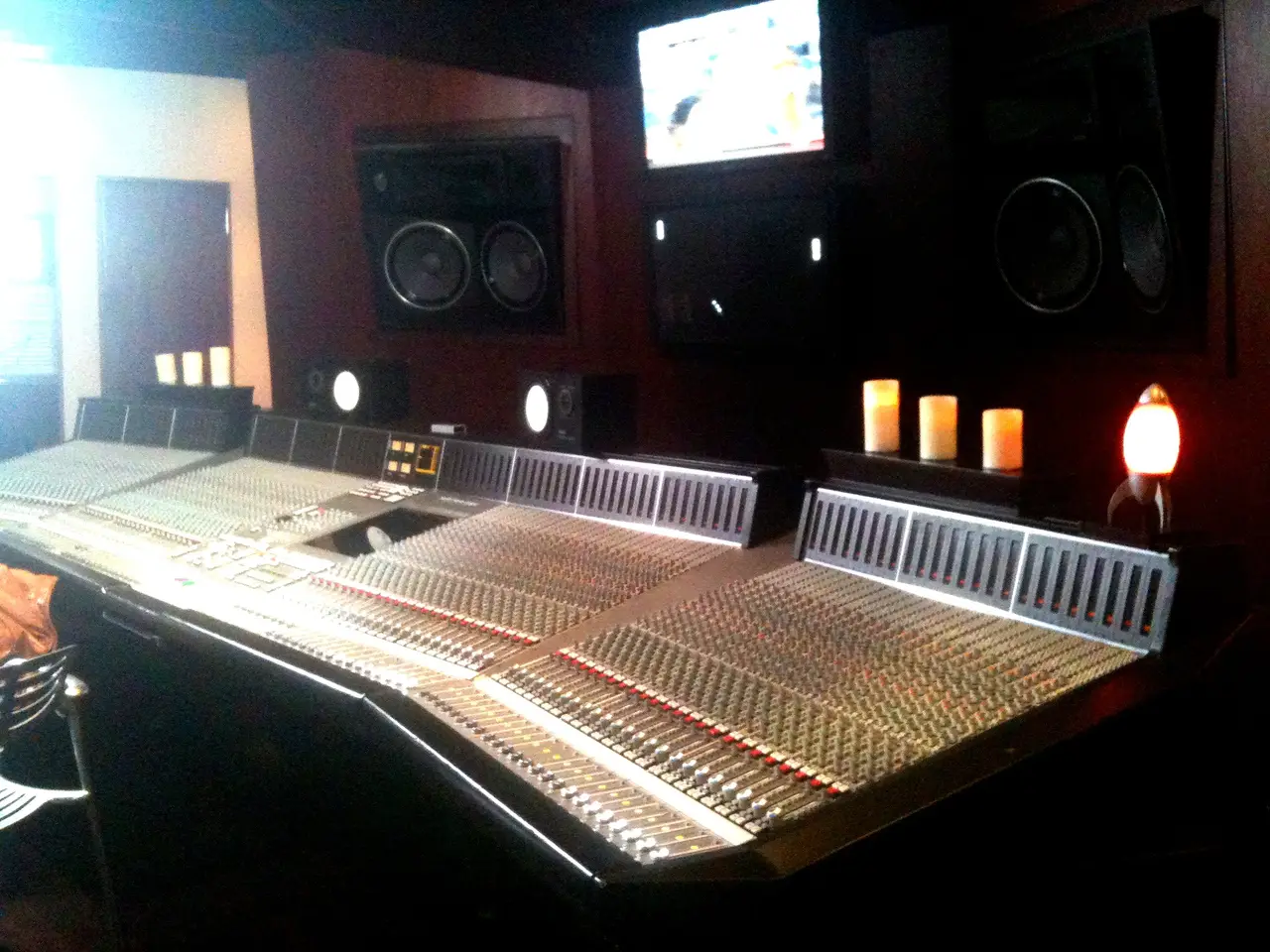 Consola grande de estudio con monitores y velas encendidas en una sala de control tenue.